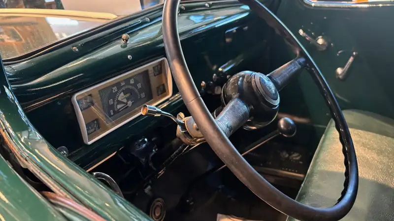 The steering wheel and dashboard of a vintage green pickup truck.