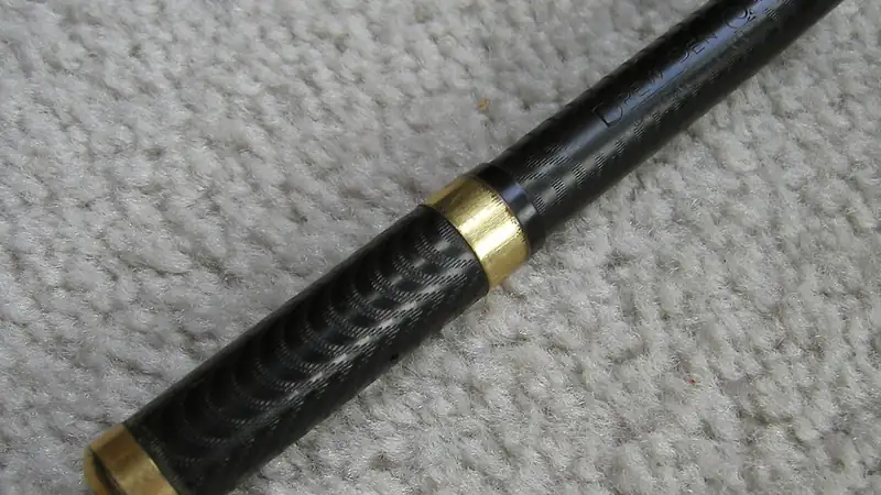 A black fountain pen with gold bands lying on a beige textured surface.