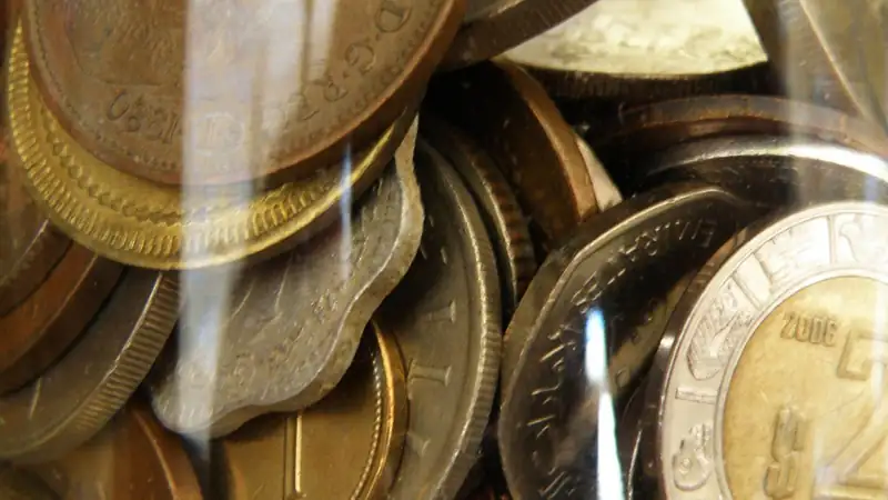 A close-up of mixed coins seen through the side of a glass jar.