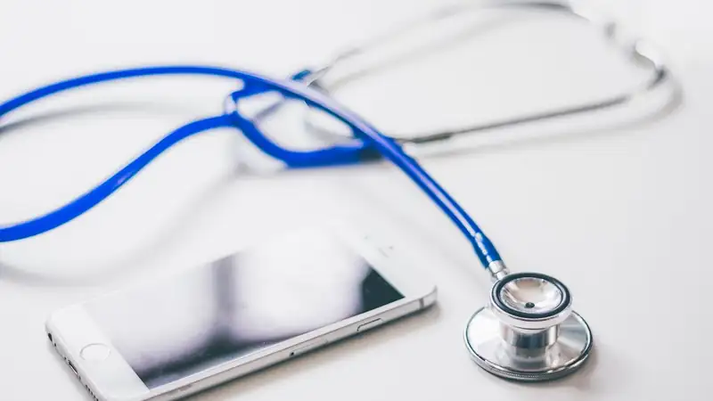 A blue stethoscope beside a smartphone on a white table.
