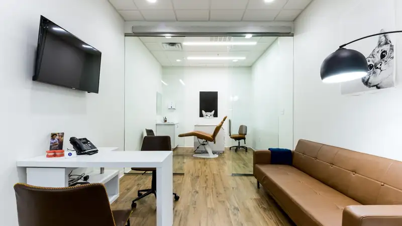 A bright modern waiting room with a leather sofa, a small desk and a glass-walled back room.