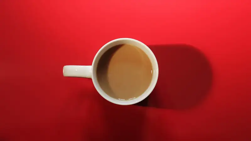 A cup of milky coffee seen from above on a bright red background.