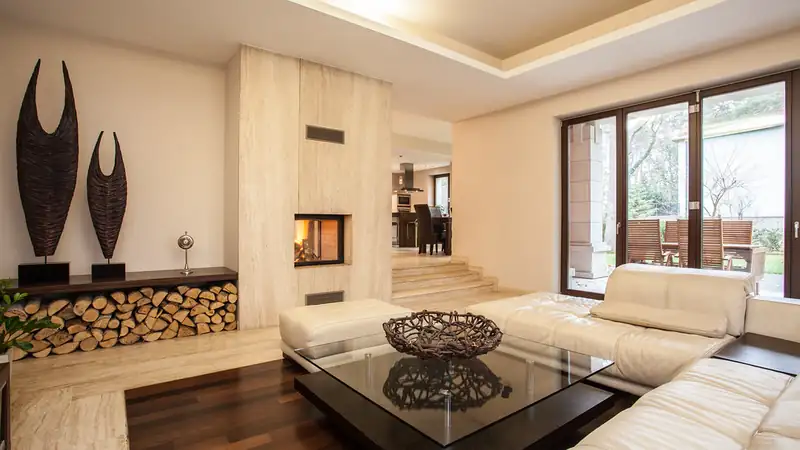 A bright living room with a white leather sofa, glass coffee table and fireplace.