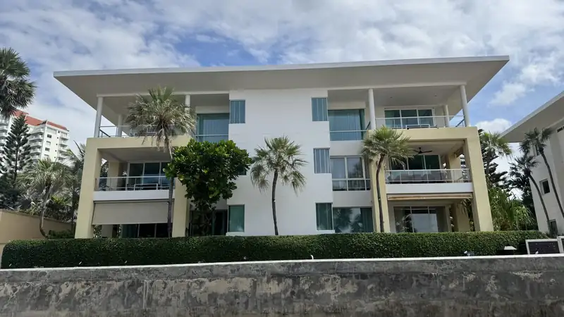 A white multi-story apartment building with balconies and palm trees under a blue sky.
