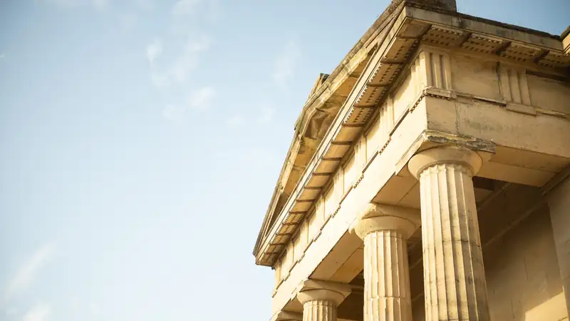 Fluted stone columns and a classical cornice seen from below against a pale sky.