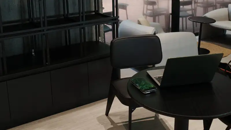 An open laptop and a smartphone on a round black table in a dim modern room.