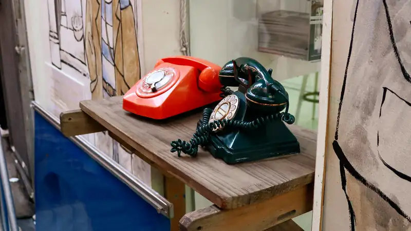 A red and a dark green rotary telephone sitting on a wooden shelf.