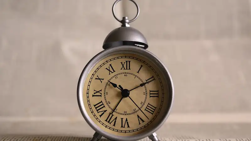 A vintage brass alarm clock with Roman numerals standing on a table.