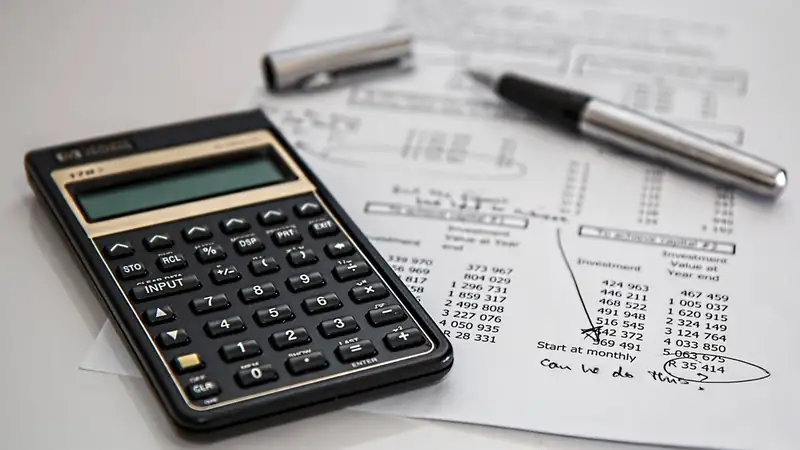 A black financial calculator and a silver pen resting on a sheet of handwritten figures.