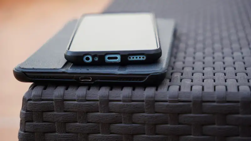 A smartphone lying on top of a tablet on a dark woven table.